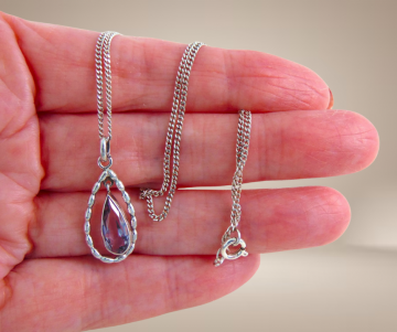 Antieke zilveren hanger druppel amethist bewegend ketting beige achtergrond 1