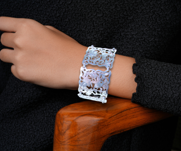 Brede antiek zilveren opengewerkte paneel armband op arm hout stoel