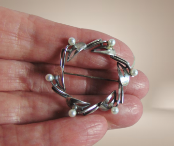 Ronde art deco zilveren broche met parels beige achtergrond