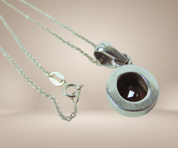 Strak zilveren ovale granaat hanger aan ketting beige achtergrond 1