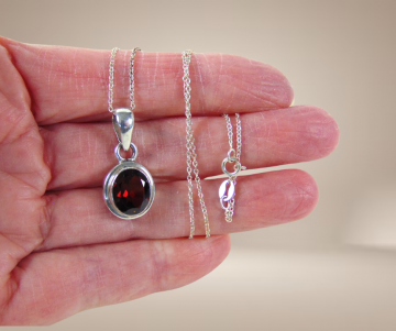 Strak zilveren ovale granaat hanger aan ketting beige achtergrond 3